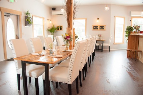 A bright, modern dining room with a long wooden table, white chairs, and decorative plants.