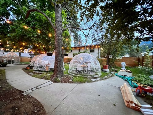 A serene outdoor space featuring geodesic domes, string lights, and a pathway surrounded by trees and greenery.