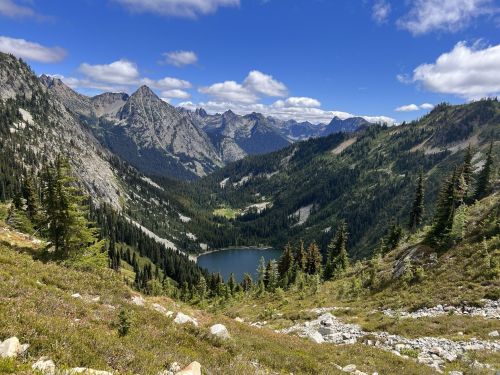 A scenic mountain landscape featuring a serene lake surrounded by lush greenery and towering peaks under a blue sky.