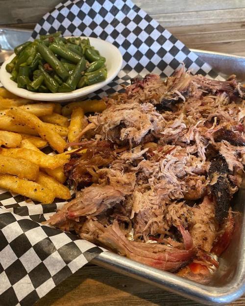 A tray of pulled pork with fries and a side of green beans on a checkered paper.
