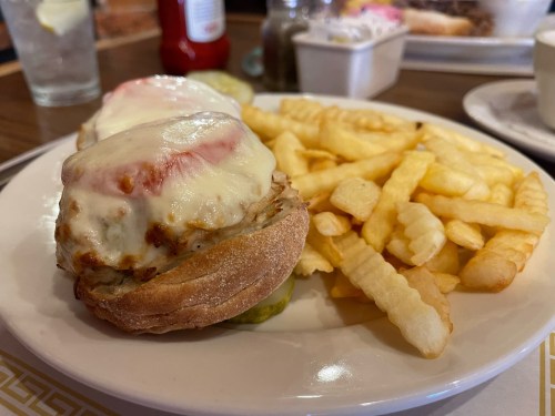 A plate with a sandwich topped with melted cheese and tomato, served with crinkle-cut fries on the side.