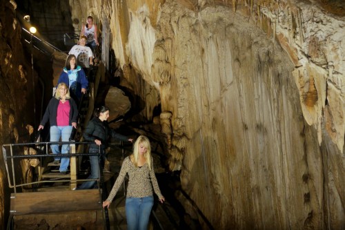 Visitors explore a cave, walking down wooden steps beside impressive rock formations.