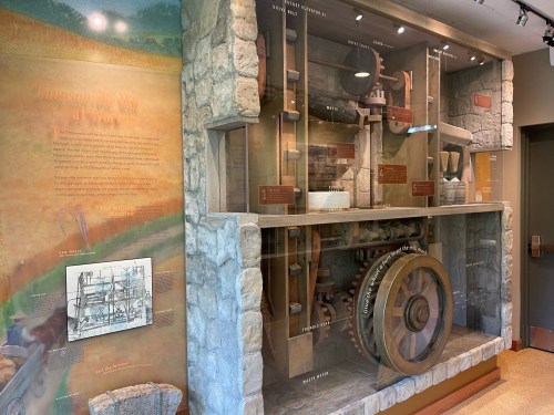 Display of historical machinery and tools, featuring a large wheel and informational panels in a museum setting.