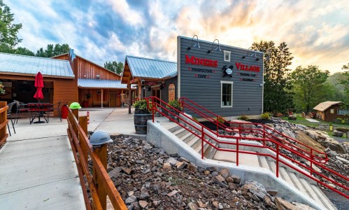 A rustic building with red accents and outdoor seating, set against a scenic sky at Miners Village.