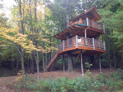 A wooden treehouse with a balcony, nestled among colorful autumn trees in a forest setting.