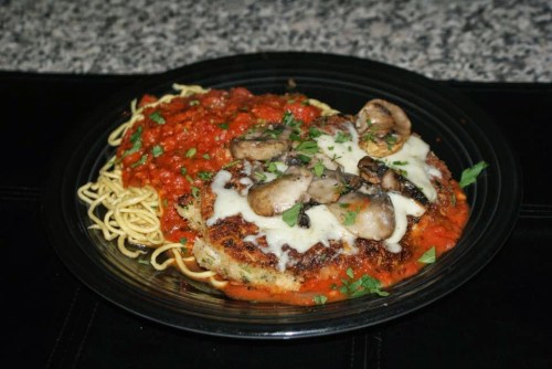 A plate of chicken parmesan topped with mushrooms, served with spaghetti and marinara sauce, garnished with parsley.
