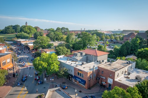 Aerial view of a vibrant downtown area with shops, trees, and a crowd enjoying a sunny day.