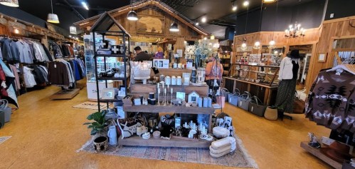 A cozy retail store interior featuring clothing, home decor, and a central display of candles and accessories.