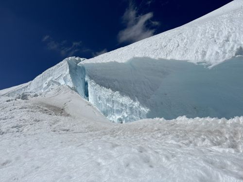 A snowy mountain landscape featuring a large ice formation against a clear blue sky.
