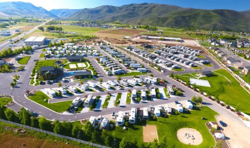 Aerial view of a large RV park with numerous parked RVs, green spaces, and surrounding mountains.