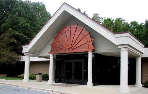 A building entrance featuring a large decorative wooden fan design above double glass doors, surrounded by columns.