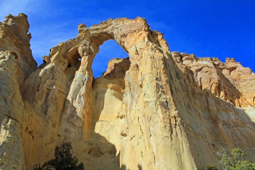 A towering rock formation with a natural arch against a bright blue sky.