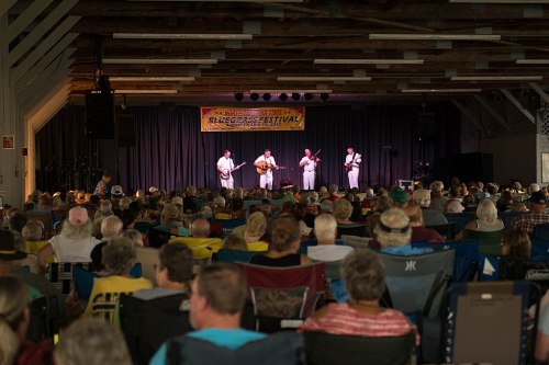 A lively music performance at a festival, with a large audience seated in folding chairs, enjoying the show.