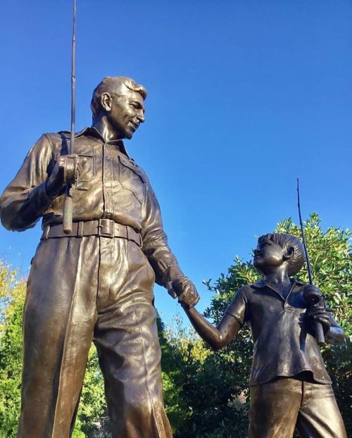 A bronze statue of a man and a boy holding fishing rods, standing together against a clear blue sky.