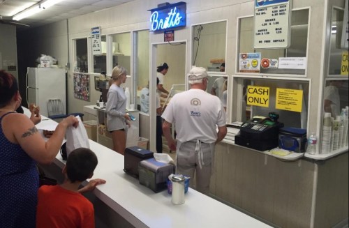 A busy counter at a casual eatery with customers ordering food and staff preparing orders in a bright, inviting space.