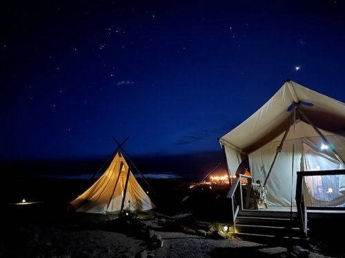 A serene night scene featuring two tents under a starry sky, with distant lights illuminating the horizon.