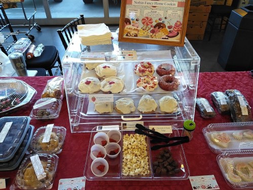 A display of assorted baked goods, including cookies, donuts, and popcorn, on a table with a red tablecloth.