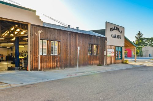 A wooden building with a sign reading "Oakdale Garage," featuring large windows and a sunny exterior.