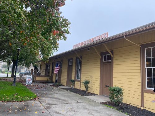Exterior of the Mobile Cowboy Museum, featuring a yellow building, American flag, and an "Open" sign.
