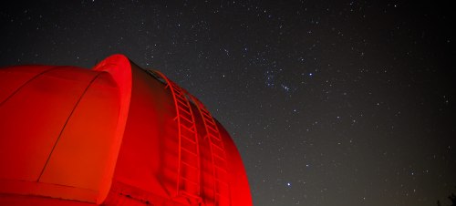 A red observatory dome against a starry night sky filled with twinkling stars.