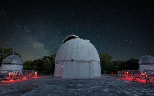 A dome-shaped observatory under a starry night sky, with red lights illuminating the surrounding area.