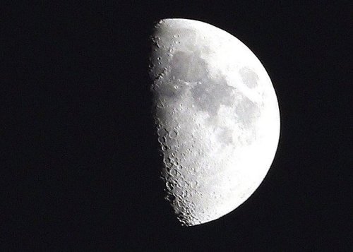 A close-up view of a half moon against a dark sky, showcasing its craters and surface details.