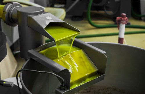 A metallic funnel pouring bright green liquid into a large container in an industrial setting.