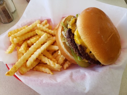 A juicy cheeseburger with lettuce, pickles, and crinkle-cut fries on a red tray.
