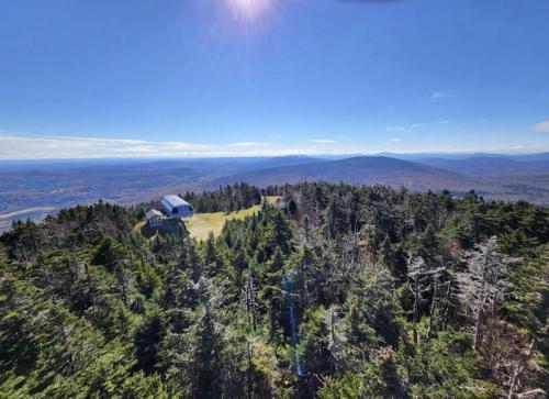 A panoramic view of a mountainous landscape with dense trees and a small building under a clear blue sky.