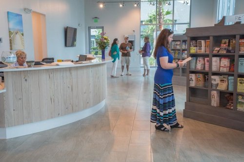 A woman in a blue top and striped skirt browses a display while others chat near a reception desk in a bright lobby.