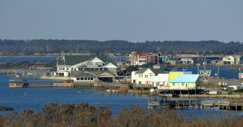 A scenic view of a waterfront area with buildings, docks, and calm water under a clear blue sky.