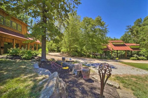 A scenic view of a rustic property with a wooden building, garden area, and sculptures under a clear blue sky.