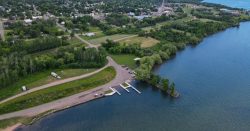 Aerial view of a lakeside area with a parking lot, boat docks, and lush greenery along the shoreline.