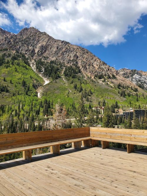 A wooden deck overlooks a lush green mountain landscape under a blue sky with scattered clouds.