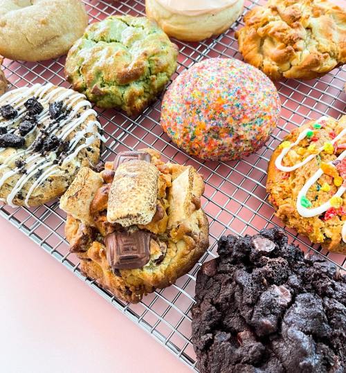 A variety of colorful cookies on a cooling rack, including chocolate, sprinkles, and s'mores flavors.