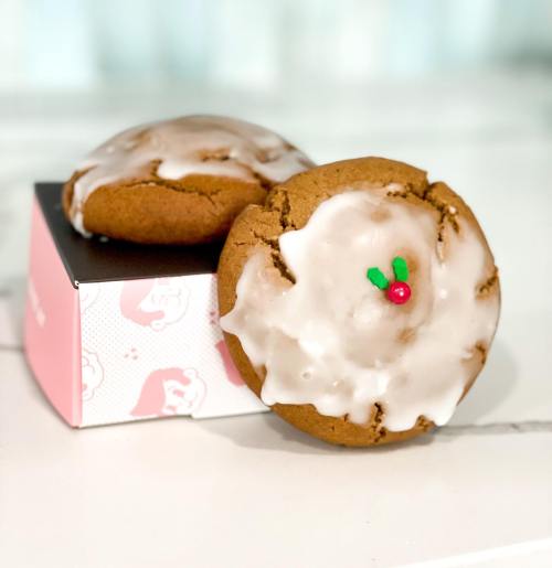Two festive cookies with icing and decorative holly, placed on a small black box.