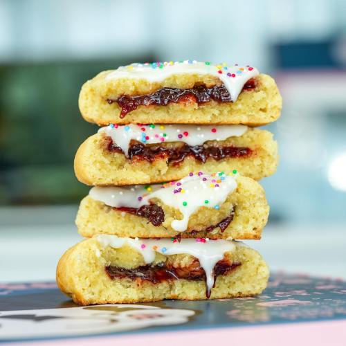 Four stacked pastries filled with jam and topped with icing and colorful sprinkles.