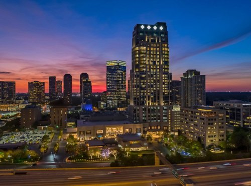 City skyline at sunset, featuring tall buildings and a vibrant sky with hues of orange, pink, and blue.