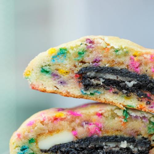 Close-up of a colorful cookie with sprinkles, revealing an Oreo cookie inside.