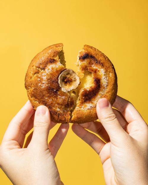 A person holds a split cookie revealing a gooey center, against a bright yellow background.
