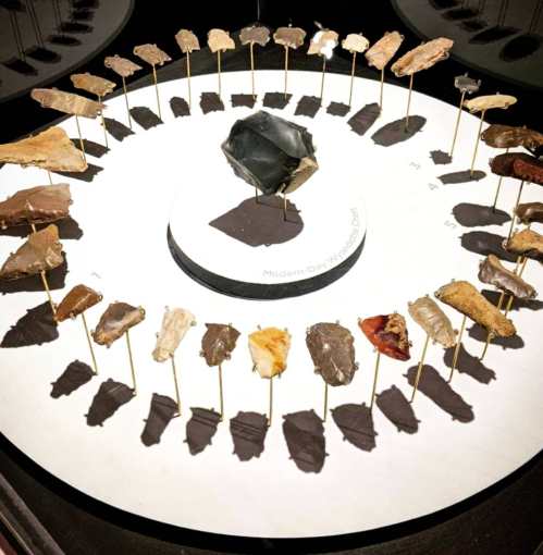 A circular display of various stone artifacts arranged around a central piece, showcasing their shadows on a base.
