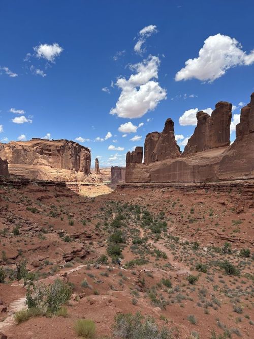 A vast desert landscape with towering rock formations under a blue sky dotted with clouds.