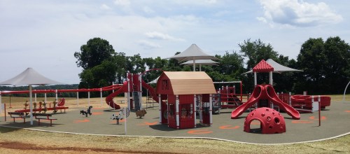 A colorful playground with slides, climbing structures, and shaded areas, set in an open grassy field.