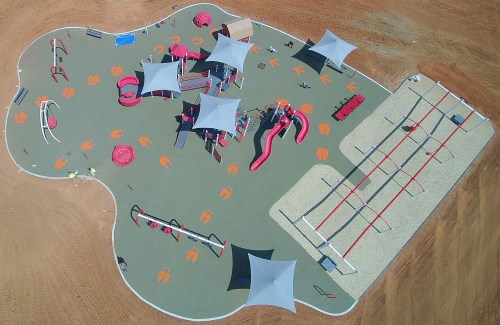 Aerial view of a colorful playground with various equipment and shaded areas on a sandy surface.
