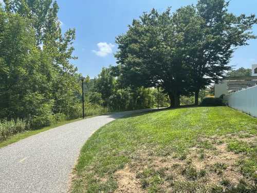 A winding path through a green park, bordered by trees and a white fence under a clear blue sky.