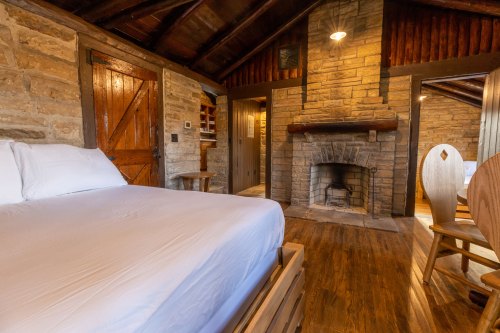 Cozy cabin interior featuring a bed, stone fireplace, wooden accents, and warm lighting.