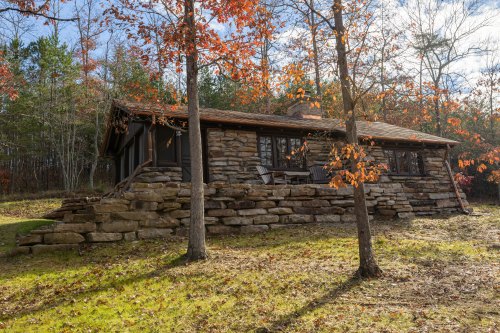 A rustic stone cabin surrounded by trees with autumn leaves, set in a serene natural landscape.