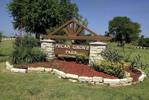 Sign for Pecan Grove Park surrounded by greenery and flowers, with a clear blue sky in the background.