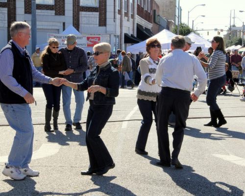 A lively street scene with people dancing and enjoying a festival atmosphere on a sunny day.