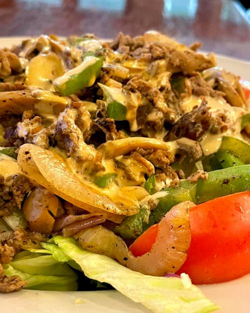 A colorful salad topped with seasoned beef, onions, green peppers, and a creamy dressing on a bed of lettuce and tomatoes.